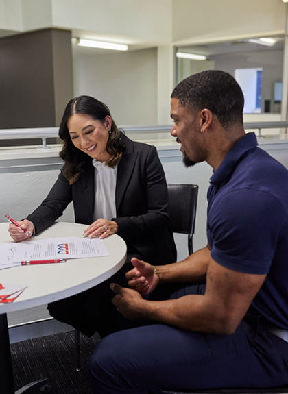 A professional woman in a black suit discussing legal documents with a client at a round table in an office setting.